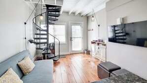 A modern living room with a spiral staircase, a flat-screen TV, and a cozy seating area. - Walk to Commercial Street! Couples Retreat w/ Deck (Provincetown)