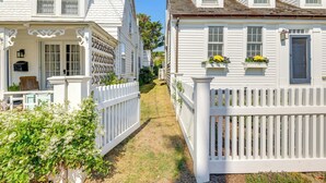 A narrow pathway between two white houses with a picket fence, a small porch, and a window with flowers. - Walk to Commercial Street! Couples Retreat w/ Deck (Provincetown)