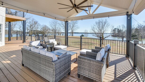 A covered outdoor deck with wicker furniture, a ceiling fan, and a view of a lake. - Lake Hartwell Home w/ Dock + Fire Pit! (Townville)