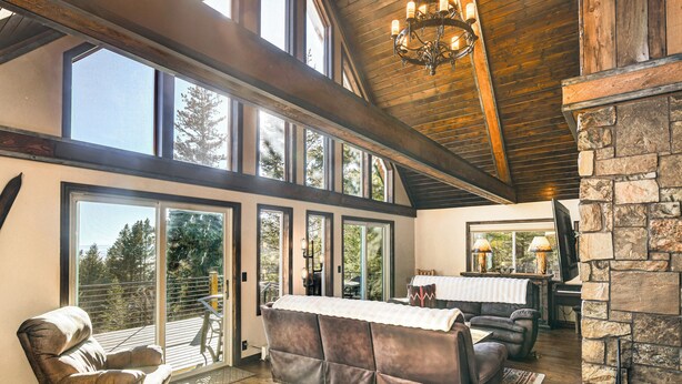 A spacious living room with a large sectional sofa, a fireplace, and a view of the outdoors through large windows. - Wyoming Cabin w/ Hot Tub & Mountain-view Deck (Thayne)
