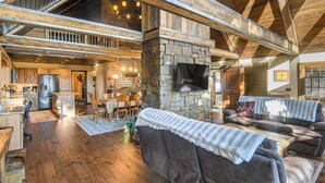 A spacious living area with a stone fireplace, wooden beams, a kitchen, and a dining area. - Wyoming Cabin w/ Hot Tub & Mountain-view Deck (Thayne)