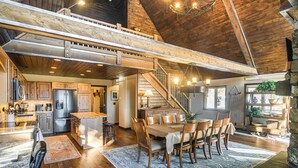 A spacious loft-style kitchen with a high ceiling, wooden beams, and a central island. - Wyoming Cabin w/ Hot Tub & Mountain-view Deck (Thayne)