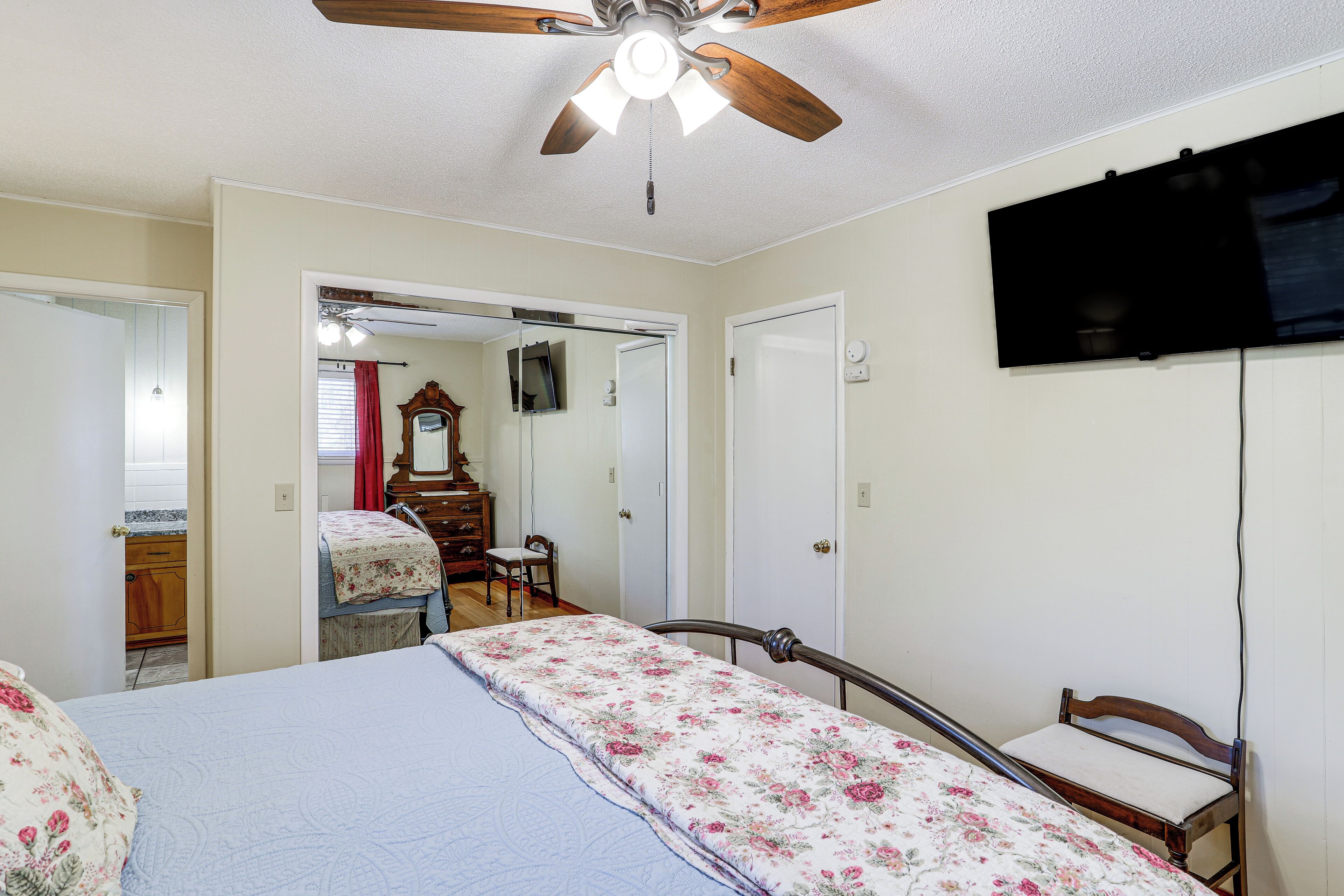 A bedroom with a bed, a ceiling fan, a television, and a door leading to another room.