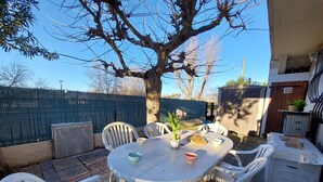 An outdoor patio with a round table and chairs, surrounded by a brick floor and a wooden fence.