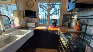 A compact kitchen with a sink, stove, microwave, and a clock on the wall.