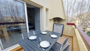 Un balcón con mesa y sillas para cuatro personas, una puerta corrediza de vidrio y un refrigerador pequeño.