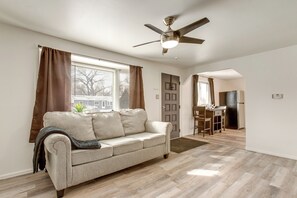 A living room with a beige sofa, a ceiling fan, and a view of a cityscape through the window.