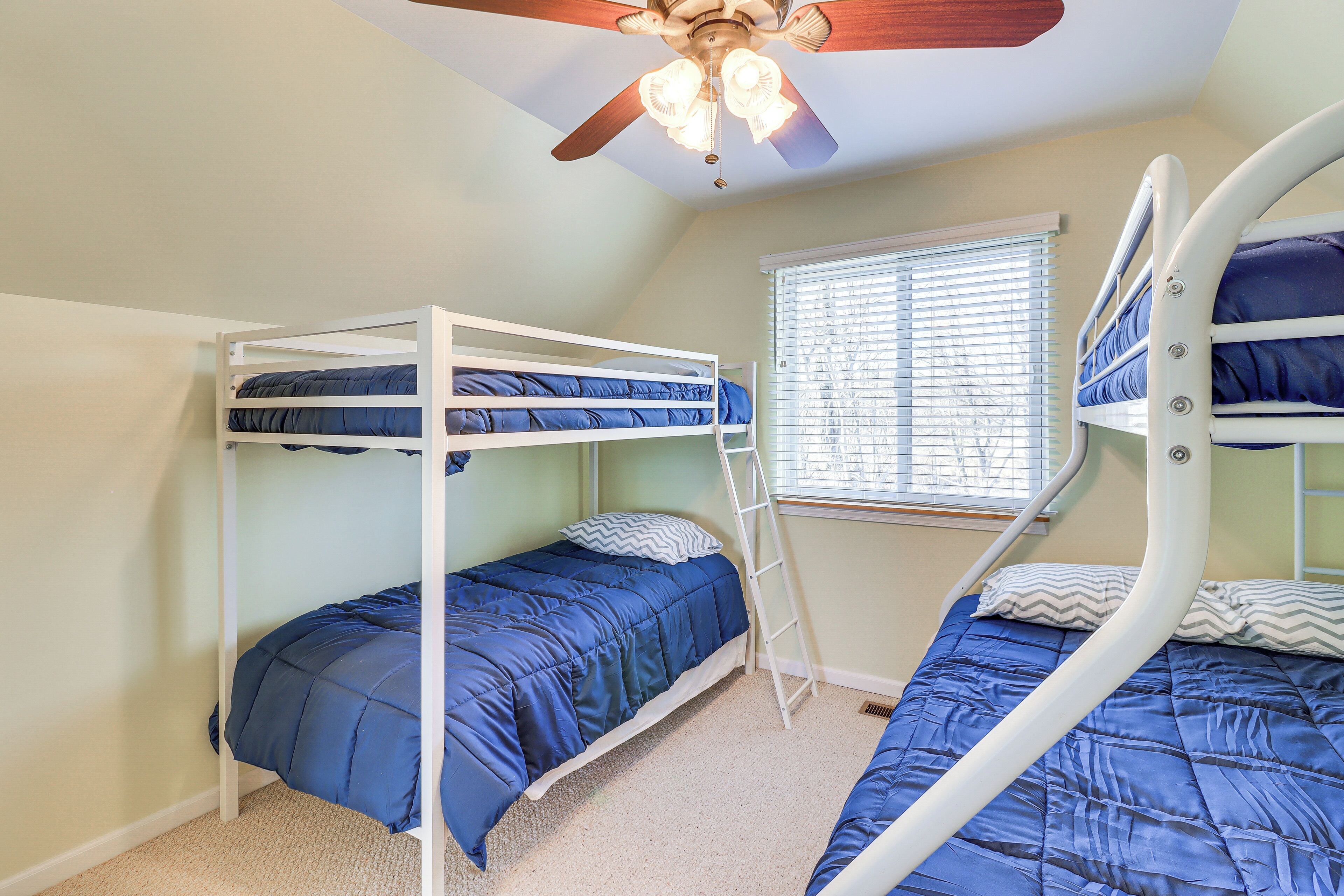 A room with bunk beds, a ceiling fan, and a window with blinds.