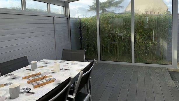 A modern patio with a table set for dining, large windows offering a view of the garden, and a clear sky. - Seaside House with WIFI, Veranda, and Parking – 320m from the Beach in Trégastel (Trégastel)