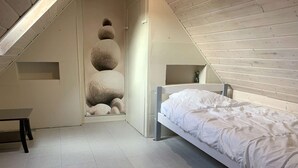 A bedroom with a sloped ceiling, a bed, a small table, and a wall with stacked stones. - Seaside House with WIFI, Veranda, and Parking – 320m from the Beach in Trégastel (Trégastel)