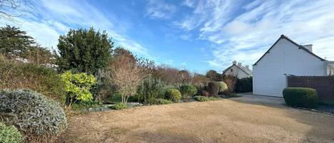 A residential property with a gravel driveway, a white garage, and a variety of shrubs and trees.