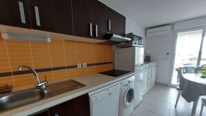 A modern kitchen with dark cabinets, a stainless steel sink, a dishwasher, and a built-in washing machine. - Charming 2-Room Cabin Apartment, 50m from Beach, A/C, Parking (Marseillan-Plage)