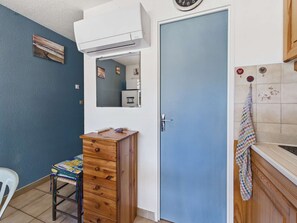 A compact kitchen with a blue door, a wooden cabinet, a white chair, and a clock on the wall.