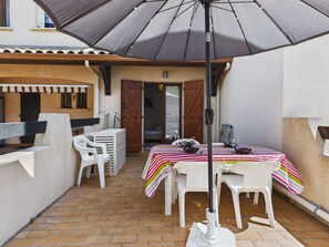 A patio with a table set for two, a grill, and a large umbrella.