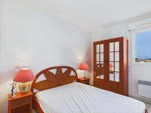 A bedroom with a bed, two bedside lamps, a wardrobe, and a window with a view. - 3-room beachfront apartment with terrace and parking, sleeps 6 (Le Grau d'Agde)