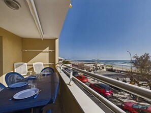 A balcony with a table set for dining, overlooking a beach with parked cars and a clear sky. - 3-room beachfront apartment with terrace and parking, sleeps 6 (Le Grau d'Agde)