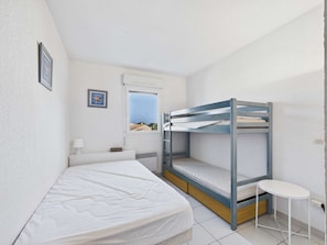 Ein Einzelzimmer mit Etagenbett, einem kleinen Tisch, einem Fenster mit Blick und einem gerahmten Bild an der Wand.