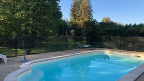 Une piscine rectangulaire dont les bords sont recouverts de petits galets, entourée d’une clôture et d’arbres.