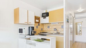 A compact kitchen with white cabinets, a microwave, a kettle, and a small sink.