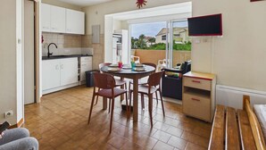 A compact kitchen with white cabinets, a dining area with a round table and chairs, and a TV mounted on the wall.