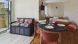 A balcony with a sofa, a dining table with chairs, a bed, and a TV.