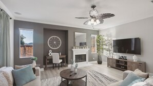 A modern living room with a fireplace, a ceiling fan, and a flat-screen TV. - 5br/3ba Home - King Beds - Fast Wifi 5 Bedroom Home by RedAwning (Victorville)