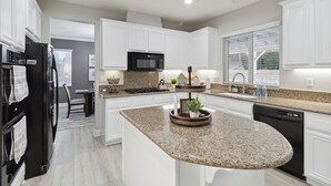 A modern kitchen with white cabinetry, granite countertops, a black refrigerator, a microwave, and a dishwasher. - 5br/3ba Home - King Beds - Fast Wifi 5 Bedroom Home by RedAwning (Victorville)