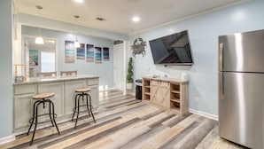 A modern kitchen with a stainless steel refrigerator, wooden bar stools, a large island with a granite countertop, and a flat-screen TV mounted above the island. - Inviting Savannah Vacation Rental w/ Game Room! (Savannah)