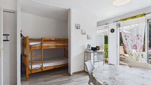 Ein Zimmer mit einem Etagenbett, einem Tisch mit einer blumigen Tischdecke, einer Kaffeemaschine und Blick ins Freie.