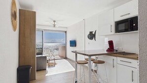 A modern kitchen with a view to the sea, a ceiling fan, and a dining area with stools. - Grau d'Agde: Studio cabin with terrace, private parking, sea view (Le Grau d'Agde)