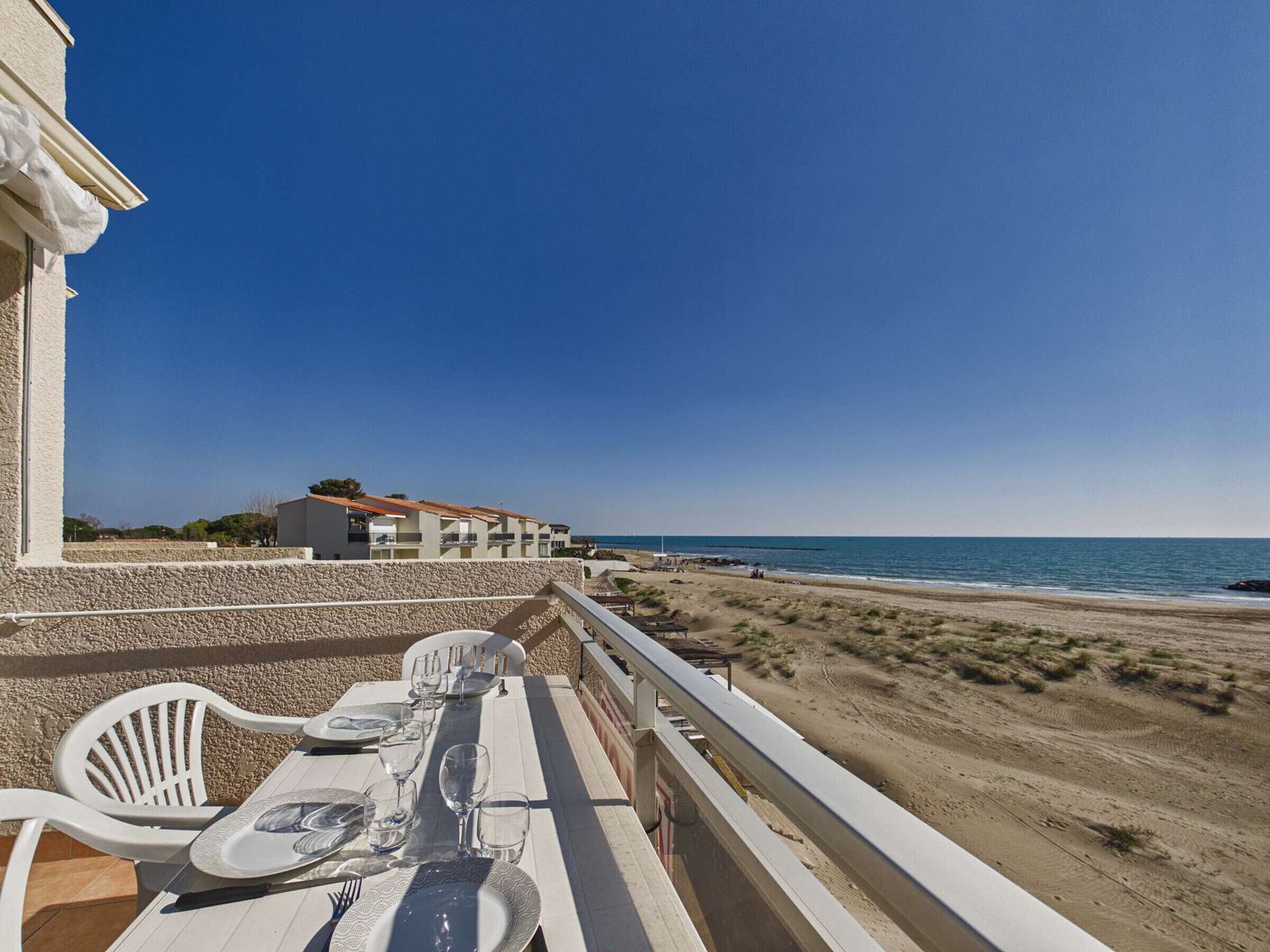 A balcony with a table set for dining, overlooking a beach and ocean.