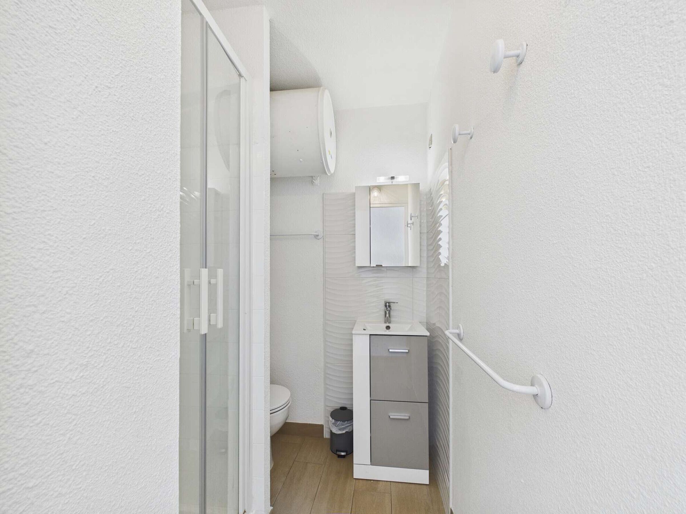A compact bathroom with a toilet, a sink, a mirror, and a shower area.