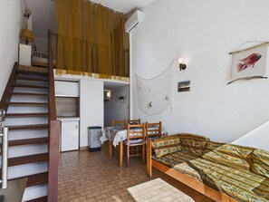 A compact room with a bed, a desk, a chair, a staircase, and a small kitchen area.