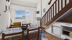 Ett kompakt bostadsutrymme med matplats, kök och en trappa som leder upp till en övre våning.