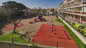 Un’area giochi con attrezzature rosse e blu, una recinzione e un edificio con balconi.