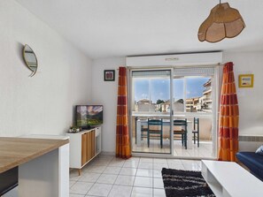 Una sala moderna con televisor, comedor y balcón con cortinas.
