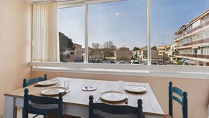 Zona pranzo con tavolo imbandito per quattro persone, una finestra con vista sugli edifici e un parapetto per il balcone.