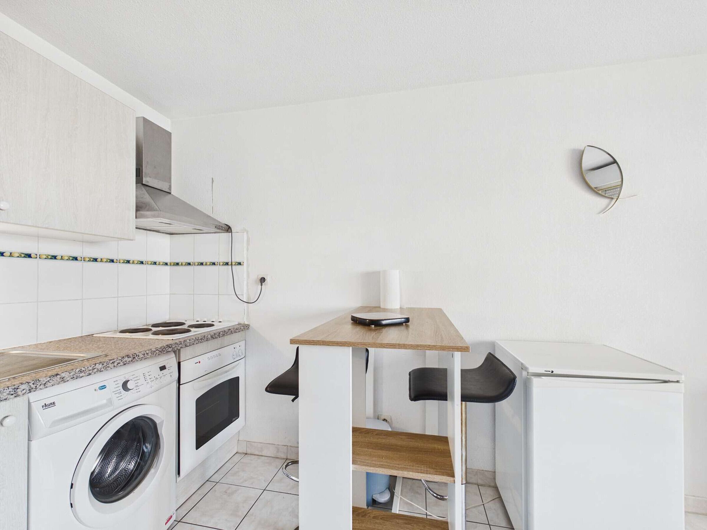 Une cuisine compacte équipée d’un lave-linge, d’une cuisinière et d’une petite table à manger avec des chaises.