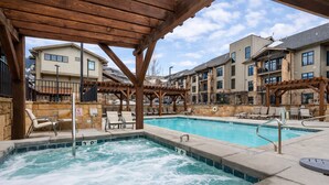 Ein Schwimmbecken mit Whirlpool, umgeben von Liegestühlen und einer Holzpergola.