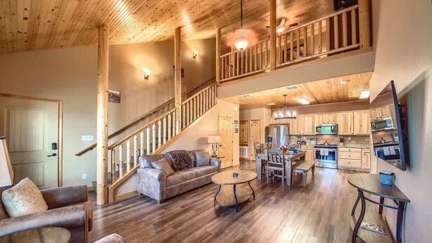 A spacious living area with a wooden staircase, a kitchen with modern appliances, and a dining area with a round table.