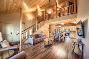 A spacious living area with a wooden staircase, a kitchen with modern appliances, and a dining area with a round table. - OM A6A8 Gruene Road Hideaway at Old Mills Resort (New Braunfels)