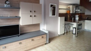 A modern kitchen with a built-in oven, a dining area with stools, and a TV on a wooden cabinet. - Duplex 3-room Apartment, 150m from Beach, Private Parking, Terrace (Marseillan-Plage)
