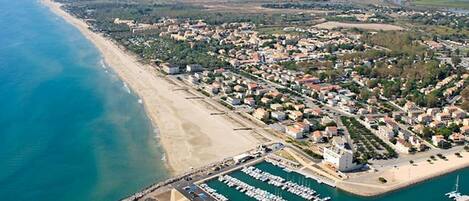 Luftaufnahme einer Küstenstadt mit Hafen, Sandstrand und Wohngebieten.