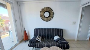 A modern living room with a striped sofa, two round wooden tables, and a decorative mirror on the wall. - Beachfront 2-Room Apartment with Direct Access, Pool, and Private Parking (Marseillan-Plage)