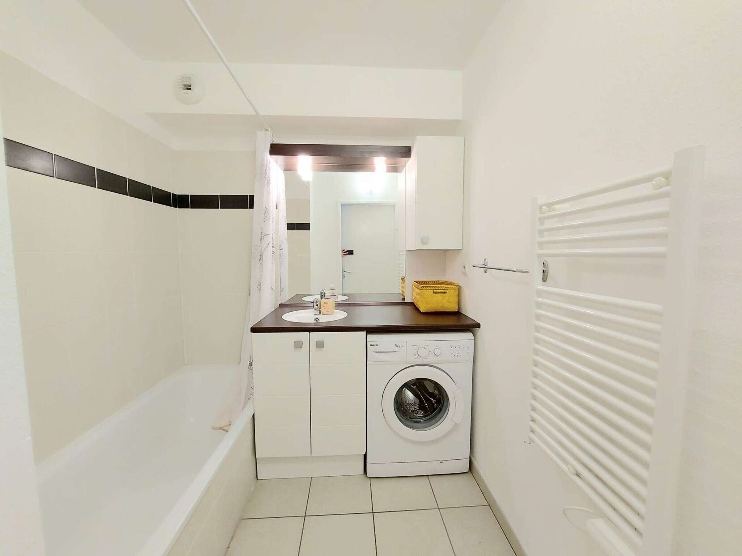 A compact bathroom with a bathtub, a washing machine, and a sink.