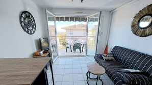 A compact living space with a sofa, a small table, a TV, and a decorative clock. - Beachfront 2-Room Apartment with Direct Access, Pool, and Private Parking (Marseillan-Plage)