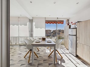A modern kitchen with a built-in oven and refrigerator, a dining area with a table and chairs, and a balcony with a view of the city.