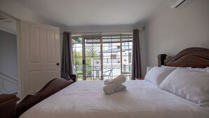 Une chambre d’hôtel avec un grand lit, une tête de lit en bois, une vue par une fenêtre ornée d’une grille en métal et une porte donnant sur une autre pièce.