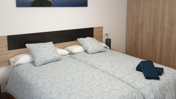 A bedroom with a bed, pillows, a nightstand, a lamp, and a wooden wardrobe. - Modern Apartment for 6 in Jaca Center, Near Cathedral (Jaca)