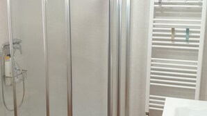 A bathroom with a glass shower enclosure, a white bathtub, and a towel rack with towels. - Modern Apartment for 6 in Jaca Center, Near Cathedral (Jaca)